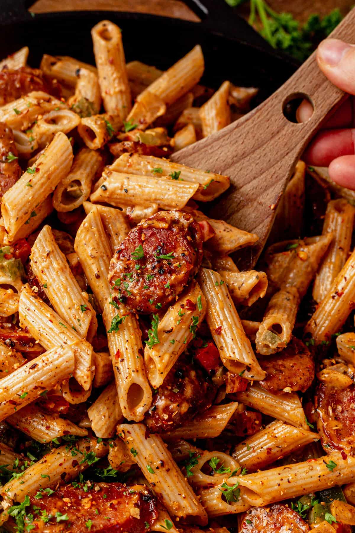 scooping cajun sausage pasta out of a pan