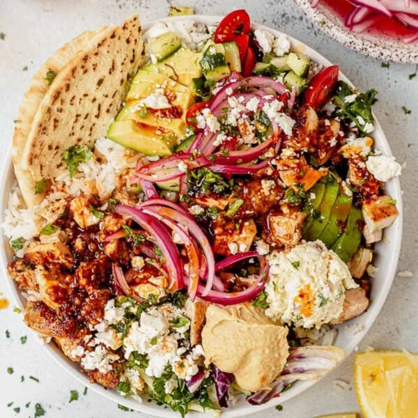 copycat cava honey harissa chicken bowl with toppings and pita