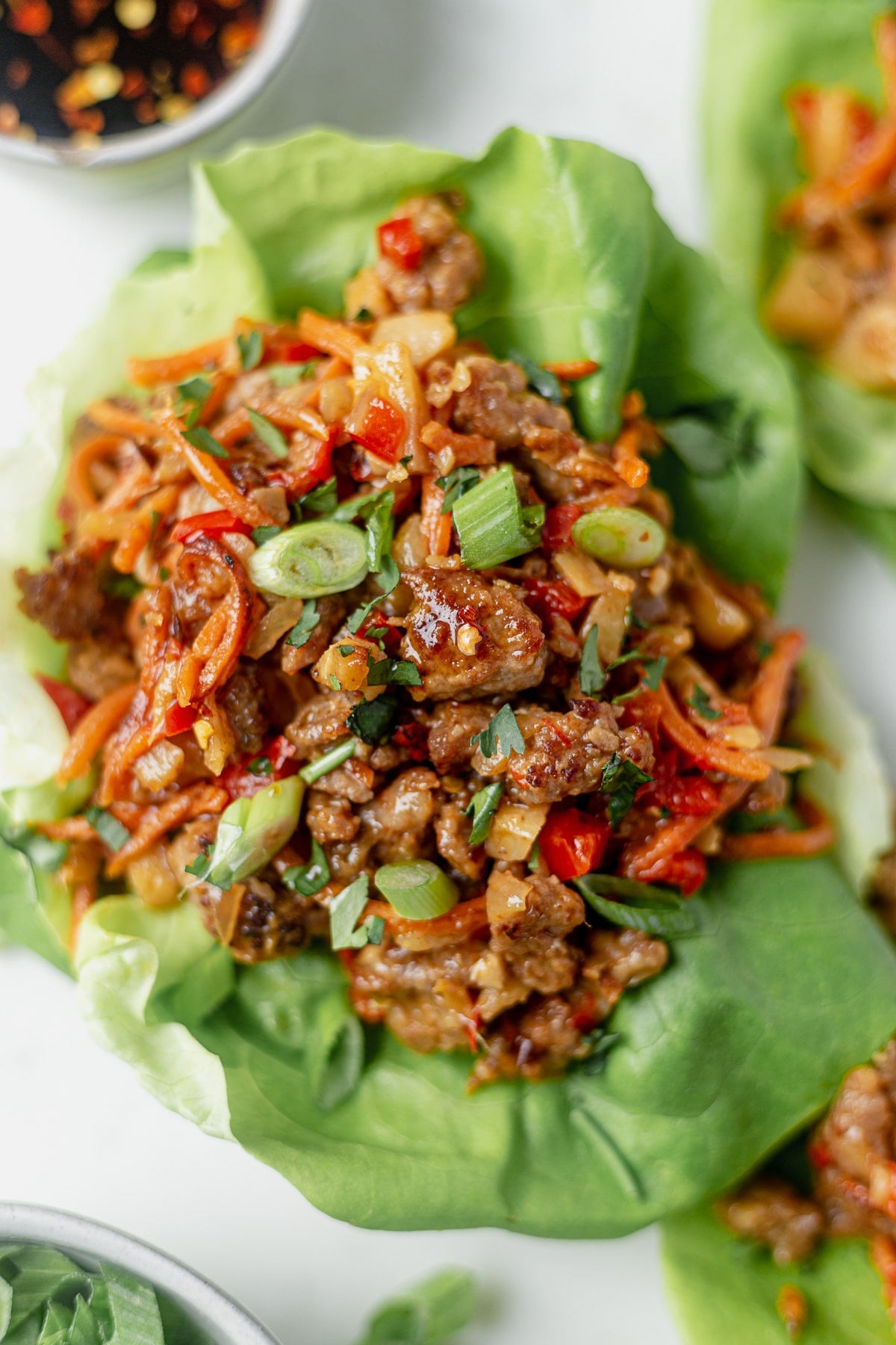 crispy pork lettuce wraps with red pepper, carrots, water chestnuts and onion in a bed of butter lettuce topped with scallions and cilantro