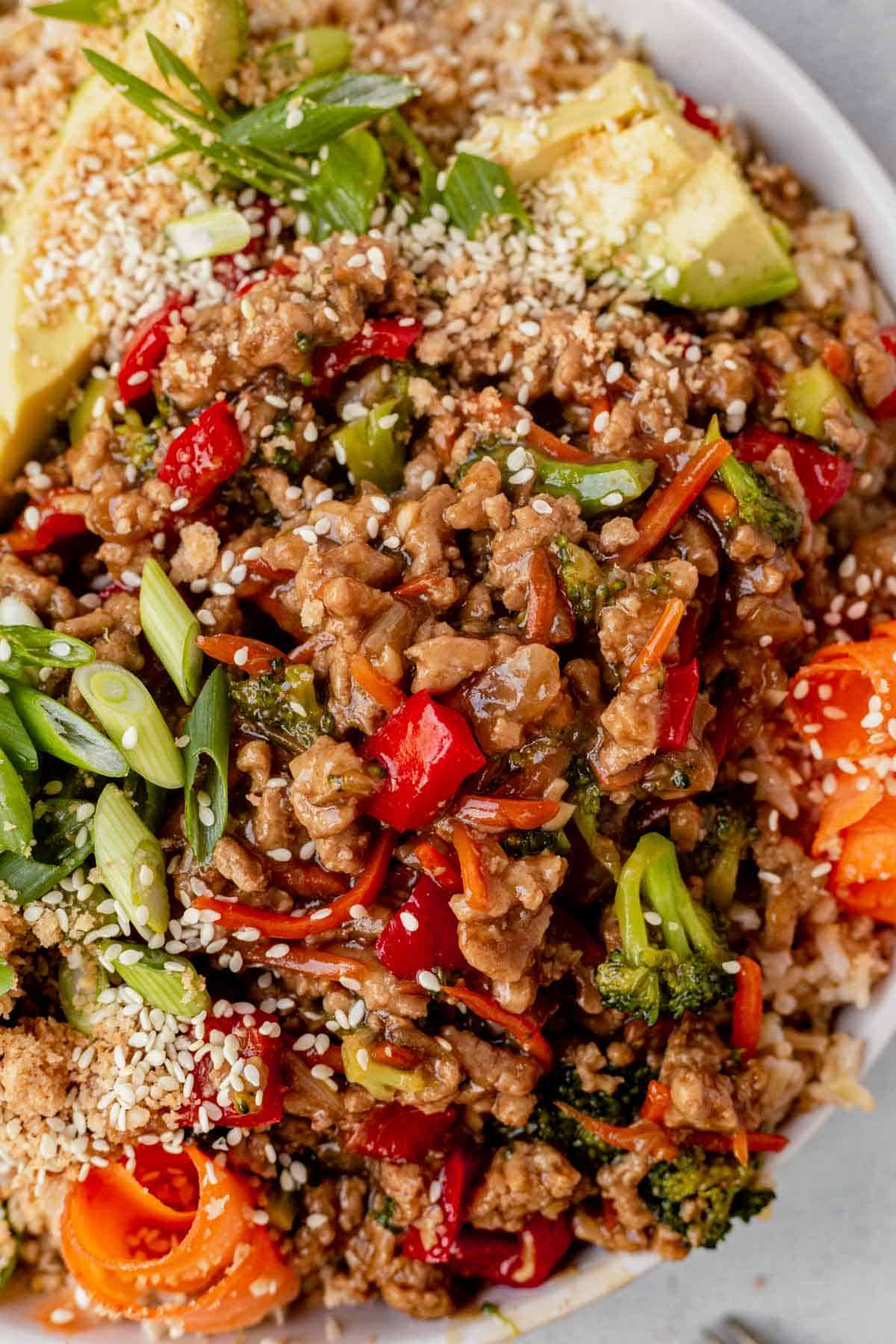 green onions, avocado, and sesame seeds on top of a teriyaki turkey rice bowl